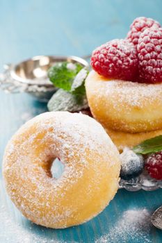 Dessert with mini donuts and berries on plate under powdered sugar on blue wooden background. Tasty donuts closeup. Doughnut. Selective focus.