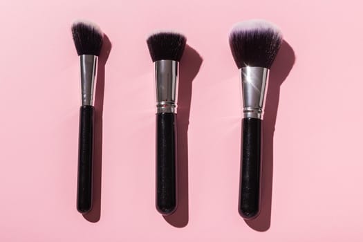 Various make-up brushes on pink background, top view. Cosmetics and beauty