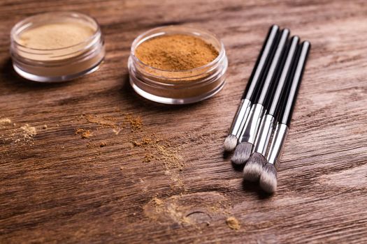 Loose compact mineral powder for face and a brushes for powder and visage on wooden background. Eco friendly and organic cosmetics