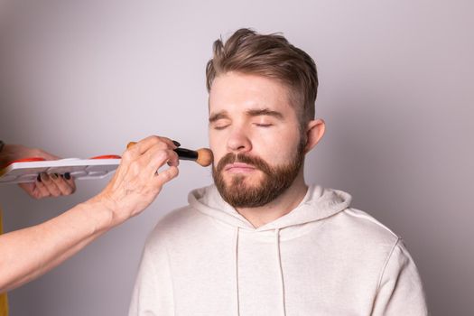 Bearded man getting makeup. Hand of visagist using brush