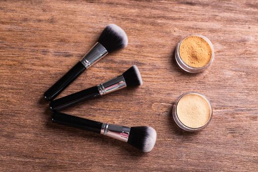 Loose compact mineral powder for face and a brushes for powder and visage on wooden background. Eco friendly and organic cosmetics