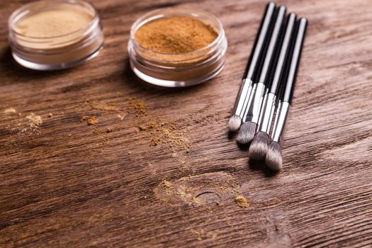 Loose compact mineral powder for face and a brushes for powder and visage on wooden background. Eco friendly and organic cosmetics