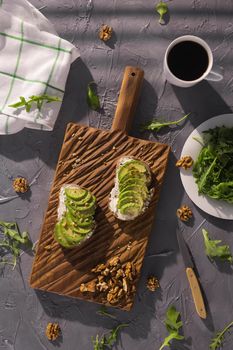 Top view of sour cream bread and avocado sandwiches with nuts and fresh herbs and cup of coffee on gray textured background. Healthy breakfast concept