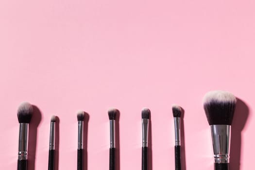 Various make-up brushes on pink background, top view. Cosmetics and beauty