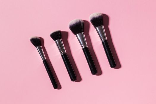 Various make-up brushes on pink background, top view. Cosmetics and beauty