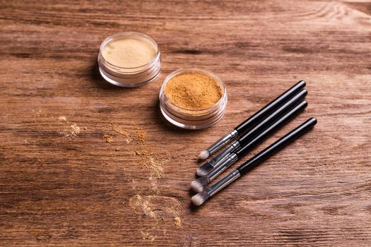 Loose compact mineral powder for face and a brushes for powder and visage on wooden background. Eco friendly and organic cosmetics