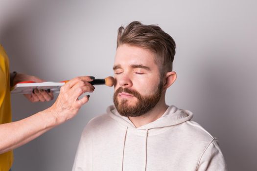 Bearded man getting makeup. Hand of visagist using brush