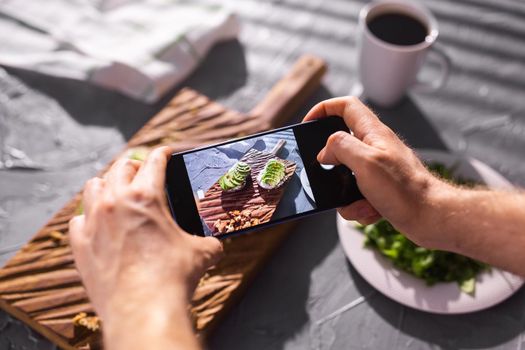 Hands take pictures on smartphone of two beautiful healthy sour cream and avocado sandwiches lying on board on the table. Social media and food