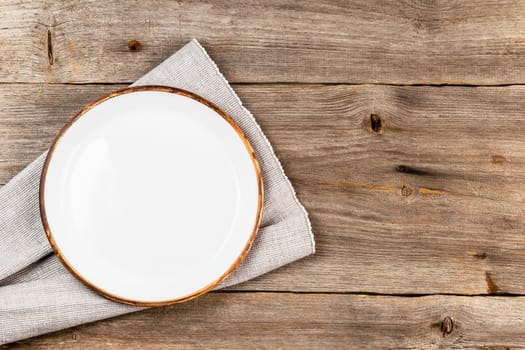 Empty white ceramic dish on rustic wooden table with cloth napkin