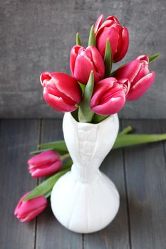 Bouquet of pink tulips in white vase on wooden background