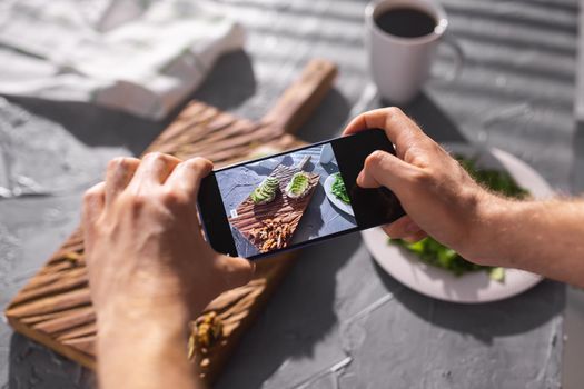 Hands take pictures on smartphone of two beautiful healthy sour cream and avocado sandwiches lying on board on the table. Social media and food