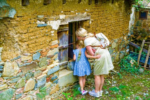 Mom and little daughter look with interest into the window of the old house.Ancient Stone Wall Made of Natural Rough Stones, Old Masonry with Cement.