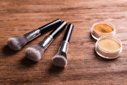 Loose compact mineral powder for face and a brushes for powder and visage on wooden background. Eco friendly and organic cosmetics