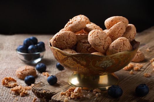 Italian almond cookie amaretti with blueberries on rustic wooden board, selective focus, law key.