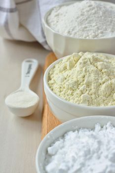 Three bowls with gluten free flour - rice flour, millet flour and potato starch and spoon with xanthan gum