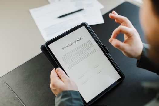 Man reading stock purchase agreement on tablet and showing ok gesture at office. Concept of filling documents.