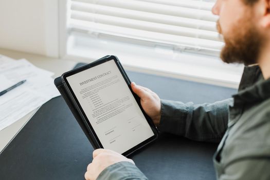 Man reading template investment contract on tablet at office. Concept of of filling documents.