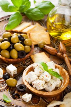 Cubed feta cheese in olive wood bowl and green and black olives on rustic wooden background. Selective focus.