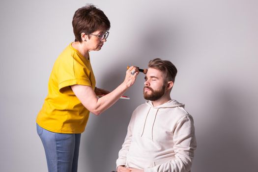 Bearded man getting makeup. Woman visagist works with brush