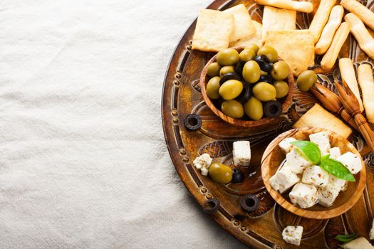 Fresh green olives in olive wood bowl and feta cheese on rustic wooden background. Selective focus. Food background with copy space.
