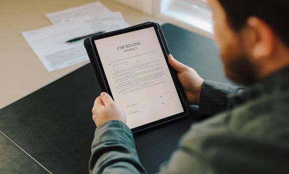 Close up man reading car selling contract on tablet at office. Concept of filling documents.