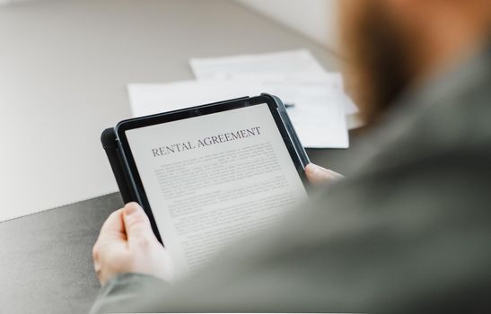 Close up businessman reading elecronic sample of rental agreement on tablet at office. Concept of lease and renting apartments, modern technology.