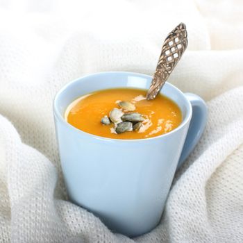 Blue cup of pumpkin soup on the knitted woolen fabric