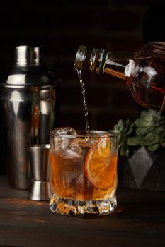 Old Fashioned in which whiskey is poured on a wooden background