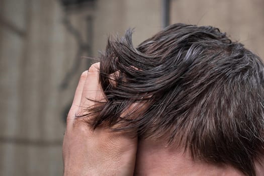 A man's hand touches his dark long hair necessary for a haircut and in need of hairdressing services.