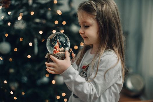Girl looking at a glass ball with a scene of the nativity of Jesus Christ in a glass ball on a Christmas tree