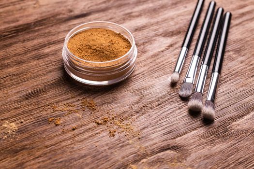 Mineral powder foundation with brush on a wooden background.