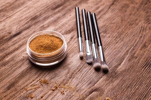 Mineral powder foundation with brush on a wooden background.