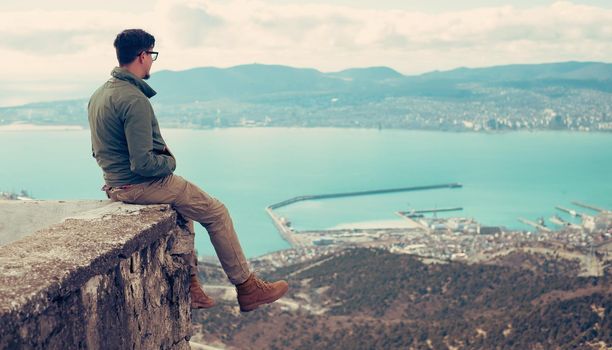 Traveler young man sitting over the sea bay and enjoying view of nature