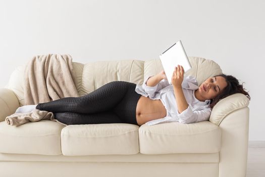 Latin pregnant woman using tablet computer sitting on sofa at home. Pregnancy and information for parenthood