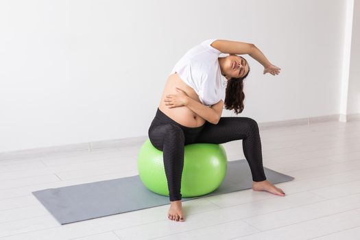 Young flexible pregnant woman doing gymnastics on rug on the floor on white background. Preparing the body for easy childbirth