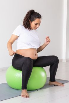 Cheerful pregnant woman dances while sitting on fitness ball. Well-being pregnancy, healthy lifestyle and positive concept