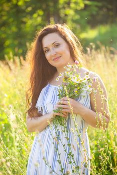 Rear view of beautiful young woman walking among wildflowers on sunny summer day. Joy of communicating with summer nature