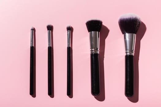 Various make-up brushes on pink background, top view. Cosmetics and beauty