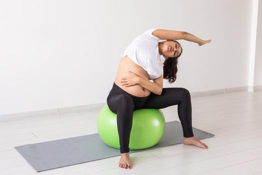 Young flexible pregnant woman doing gymnastics on rug on the floor on white background. Preparing the body for easy childbirth