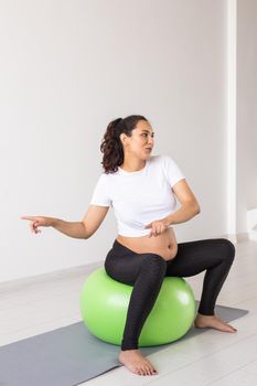 Cheerful pregnant woman dances while sitting on fitness ball. Well-being pregnancy, healthy lifestyle and positive concept