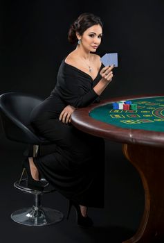 Full length portrait of sexy woman with poker cards and chips. Female player in a beautiful black dress.