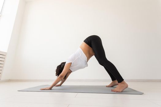 Young flexible pregnant woman doing gymnastics on rug on the floor on white background. Preparing the body for easy childbirth