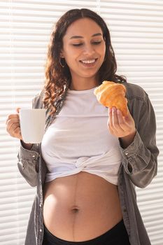 Healthy beautiful pregnant woman drinking tea and eating croissant during lunch. High-calorie nutrition while waiting for birth of baby