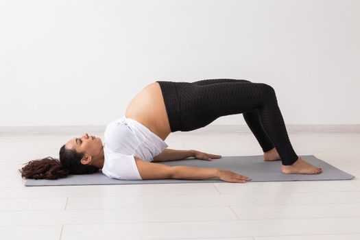 Young flexible pregnant woman doing gymnastics on rug on the floor on white background. Preparing the body for easy childbirth