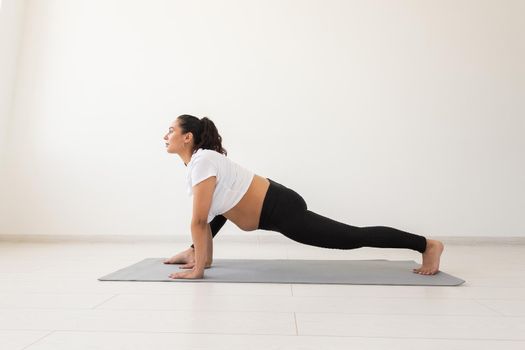 Young flexible pregnant woman doing gymnastics on rug on the floor on white background. Preparing the body for easy childbirth