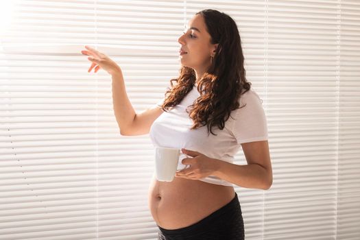 Pregnant woman eating croissant and drinks coffee. Pregnancy and maternity leave.