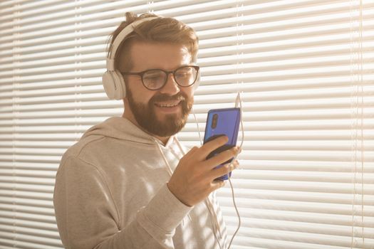 Close-up portrait of young stylish hipster man choosing favorite music in smartphone with headphones in office. Music subscription