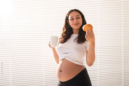 Happy pregnant woman with croissant buns at home. Pregnancy, eating and people