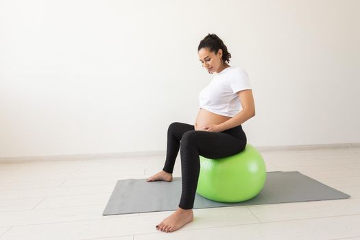 beautiful young pregnant woman doing exercise at home on fitball.