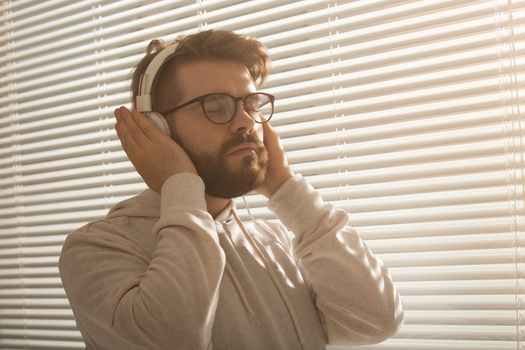 Close-up portrait of young stylish hipster man enjoying his favorite music with headphones in the office. Lunch break and positive mood concept
